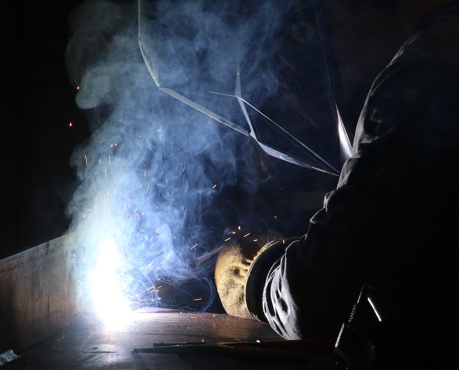 A worker welding a piece of metal onto a large flat piece of metal